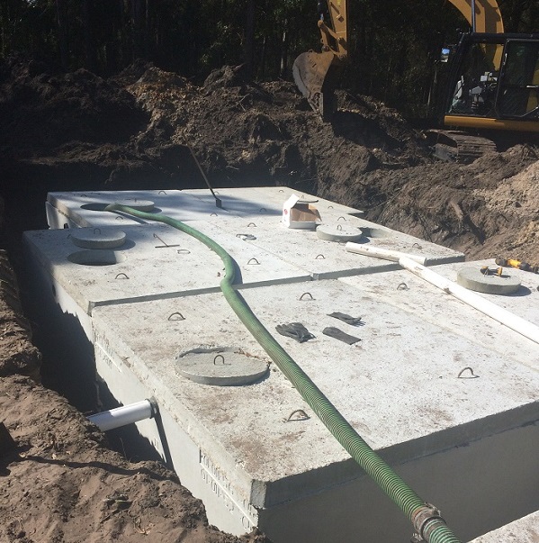 Concrete septic tank being set into an excavation with equipment visible.