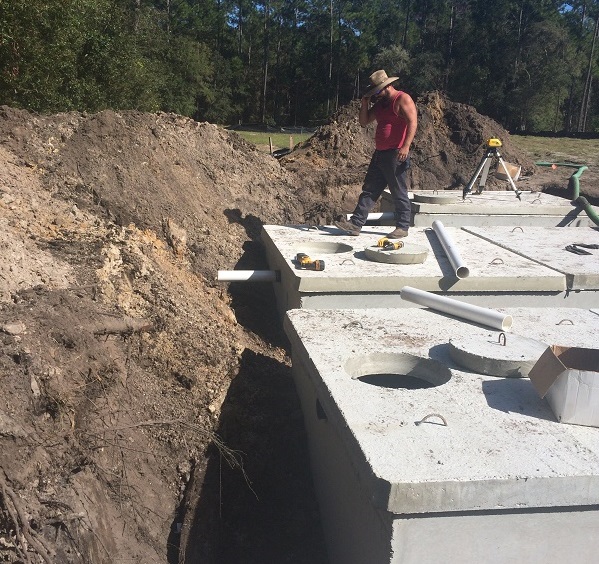 Concrete septic tank at a job site with a worker and equipment in the background.