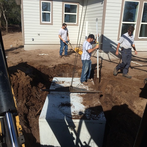 Workers and a homeowner standing around an open septic excavation beside a house.