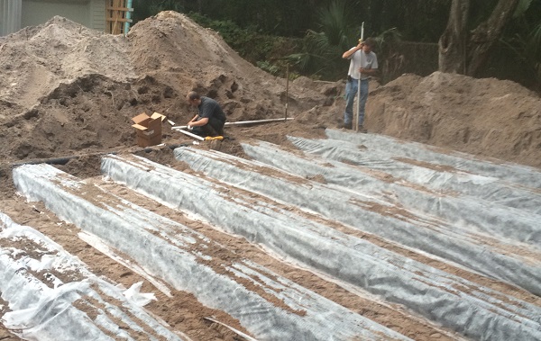 Open trenches at a drainfield installation with workers on site.